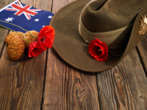 Australian flag, slouch hat and poppy laying on a wooden deck.