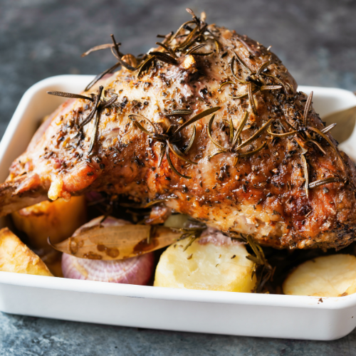 roast lamb in white baking dish surrounded by roast potatoes