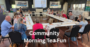 People sitting around a u shaped table smiling and eating morning tea